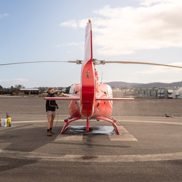 Red helicopter being washed on a Launceston helipad, rear view with rotor blades