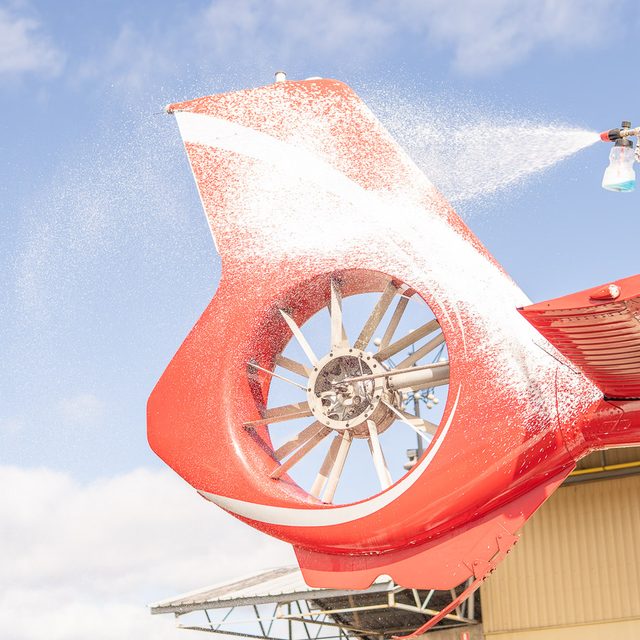 Snow foam sprayed over a helicopter tail rotor against a blue sky